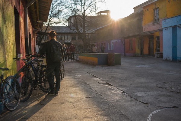 Bicycles leaning against a low painted wall in an enclosed former barracks yard, riders standing beside them, Metelkova, Ljubljana