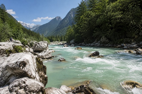 A milky green alpine river running fast between pale boulders under steep forested slopes, Soca Valley, Bovec
