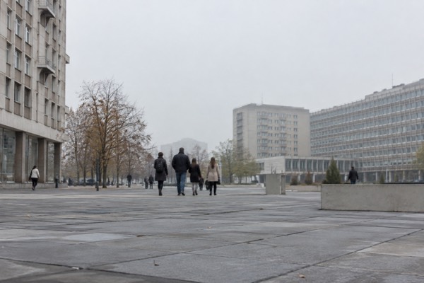Wide 1960s concrete and stone blocks along an open square, a small group crossing the paving in front of them, Bežigrad, Ljubljana