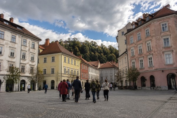 A guide with a small group on an open paved square, a wooded hill showing between the rooftops beyond, Prešeren Square, Ljubljana