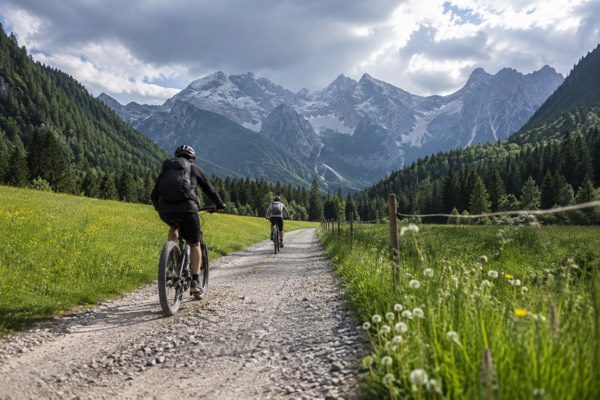 Electric bikes on a valley track at the edge of a national park, meadow either side and grey peaks ahead, Kranjska Gora, Slovenia
