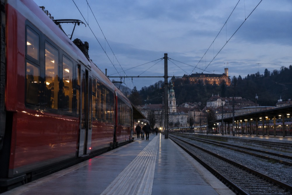 Red regional train at a Slovenian station platform with the Ljubljana skyline in the distance