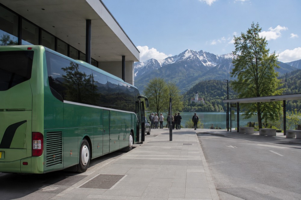 A green intercity coach parked at a bus station platform beside a modern station building