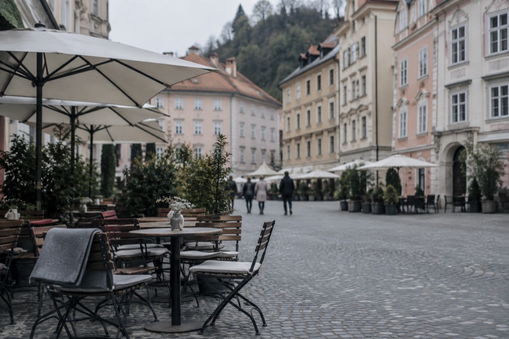 A car-free cobbled square in Ljubljana with cafe tables and pastel-coloured buildings around the edge