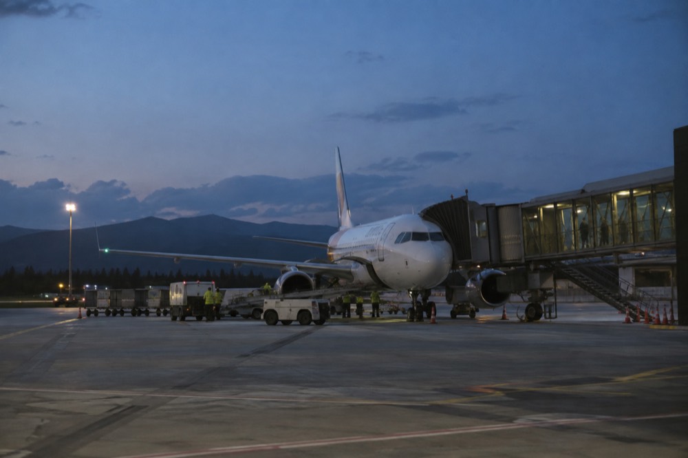 A regional airport apron at dusk with a single aircraft at the gate and ground vehicles nearby