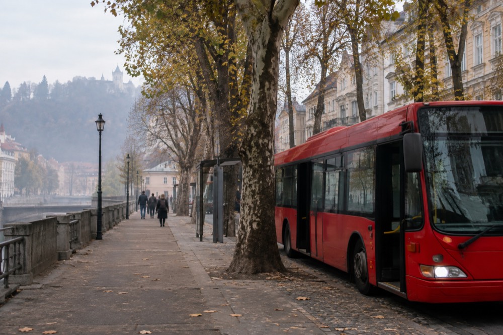 A red city bus parked at a stop beside a tree-lined street