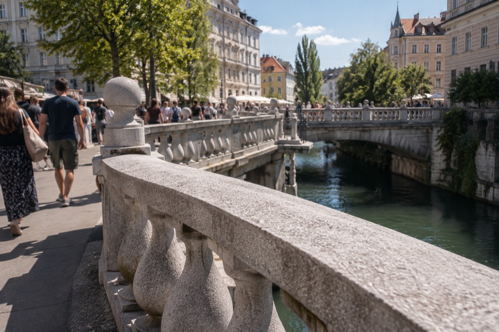 A stone triple bridge with balustrades spanning a river between old buildings