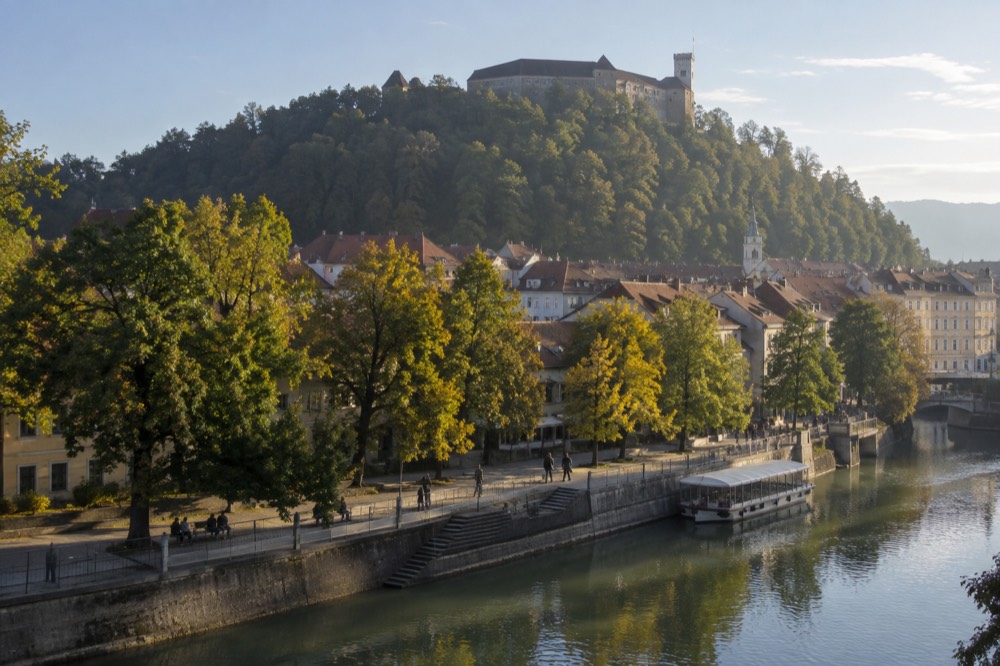 A river promenade with a moored boat and a hilltop castle in the background