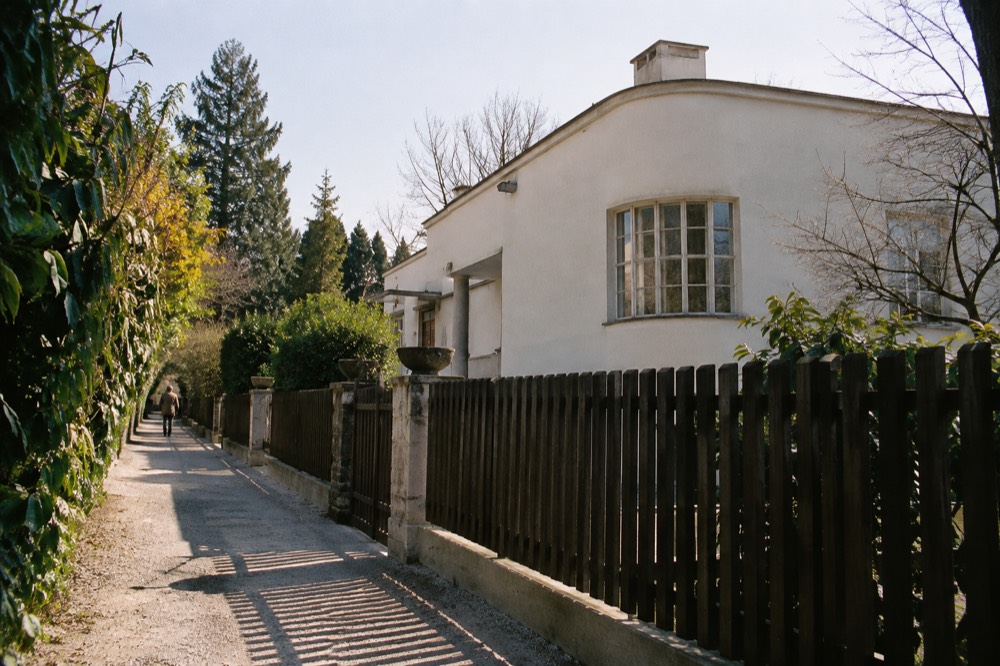 A low white villa with a round corner window and a dark timber fence under a pale sky