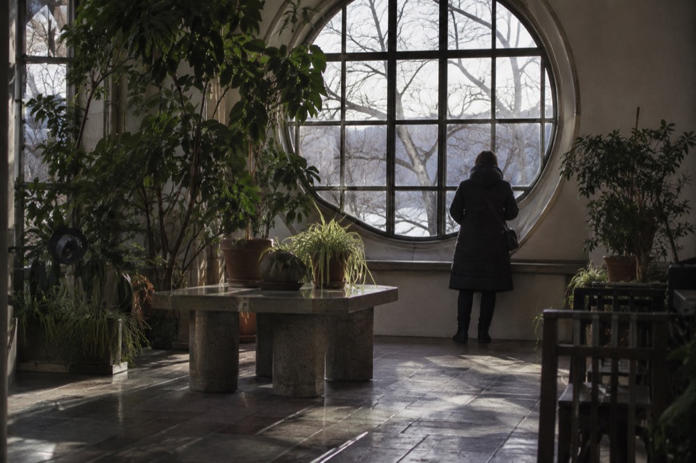 A winter garden room with tiled floors and tall plants beside a bright round window