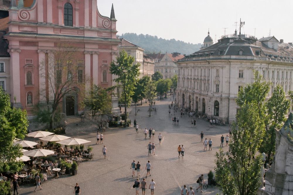 Pink church facade above an open square with outdoor cafe tables and a stone monument