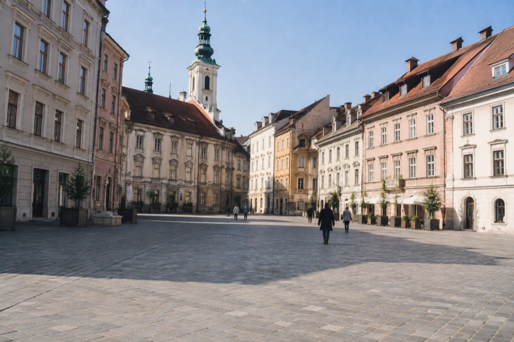 Quiet early morning square with empty stone paving and a church tower in soft light