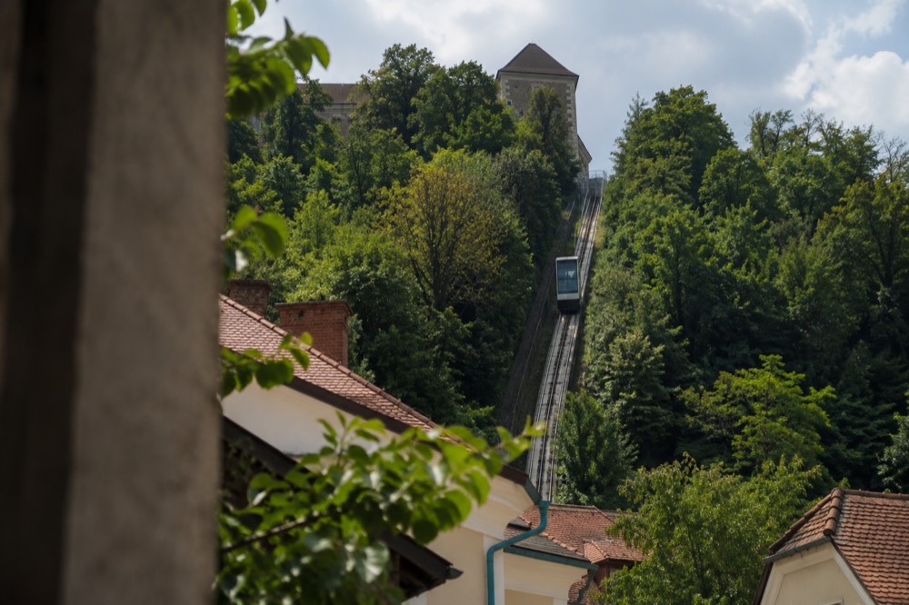 Funicular railway car ascending a wooded hill above city rooftops