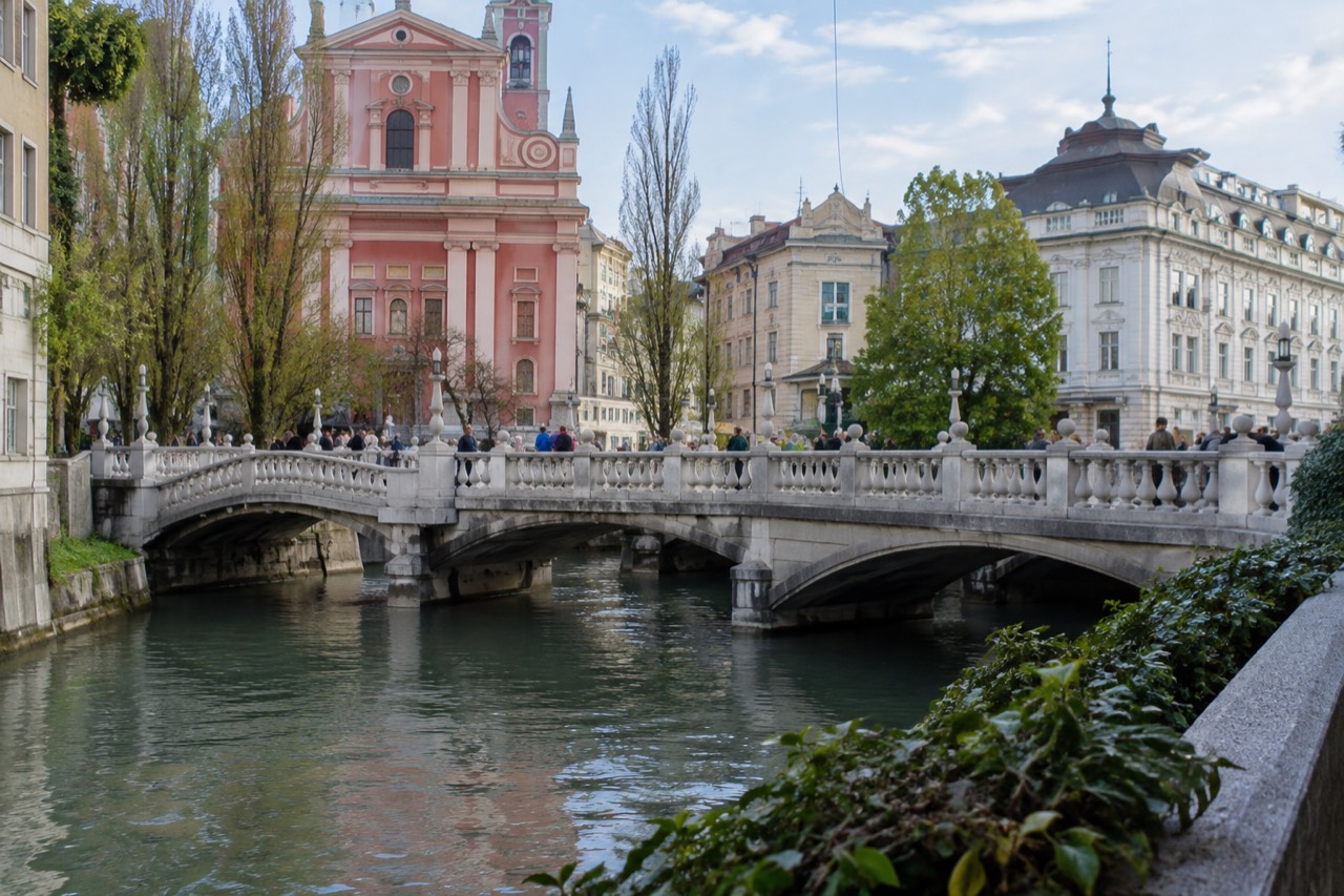 Three stone footbridges side by side across the Ljubljanica river with the Old Town behind