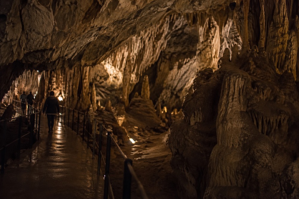 A limestone cave chamber with walkways and stalactites lit by warm lamps