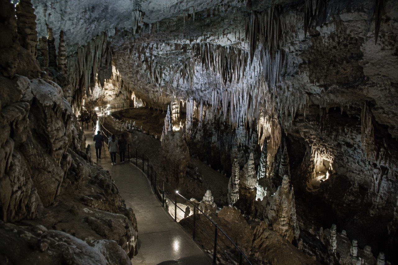 Underground chamber in Postojna Cave with stalactites lit by walkway lights