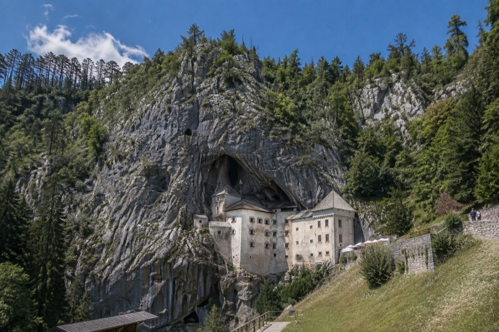 A stone dining hall inside a castle with a natural rock wall at one end