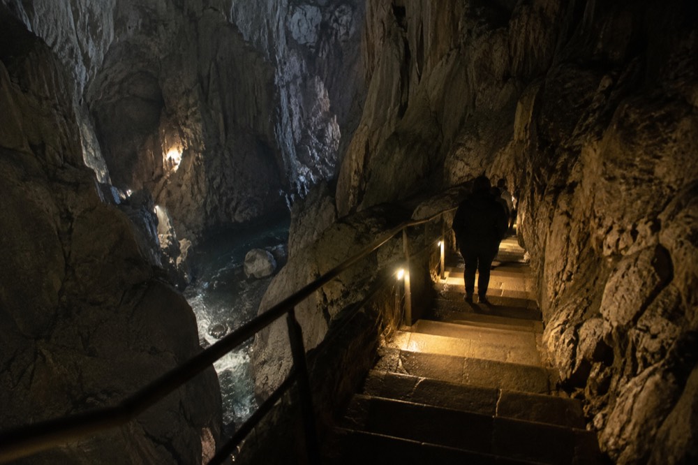 A stone stairway descending into a cave passage lit by warm lamps