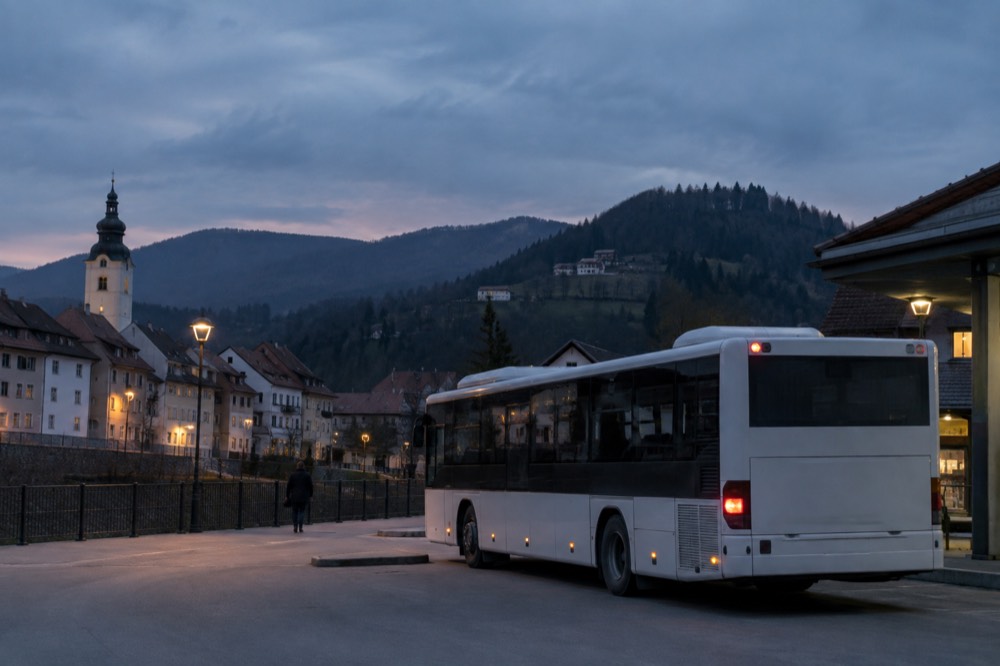 A regional bus parked at a small town terminus with hills behind it