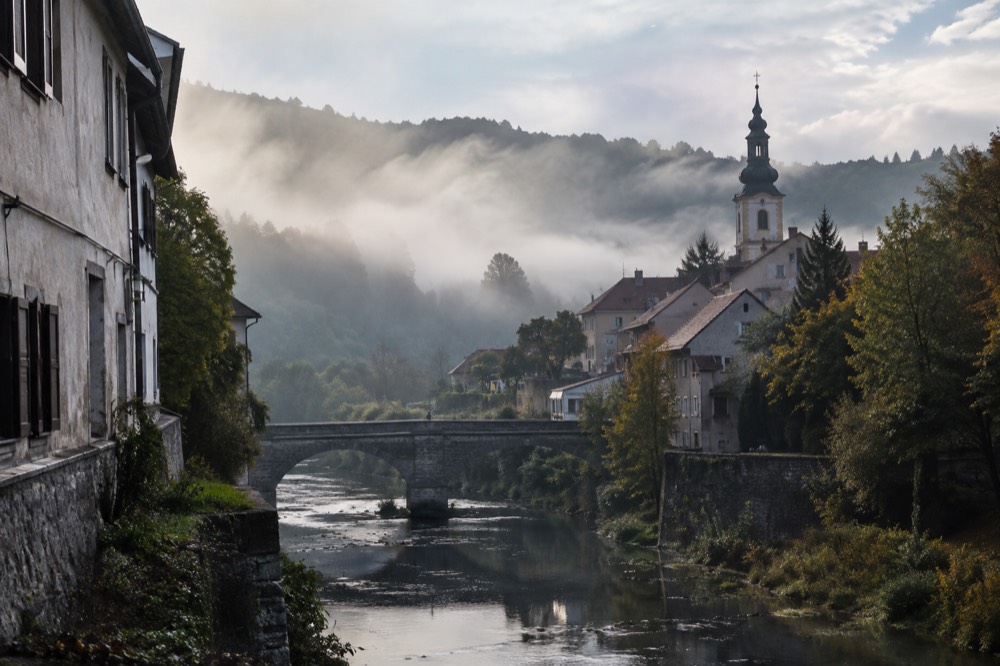 Morning mist over a river valley with a church spire rising above the fog line