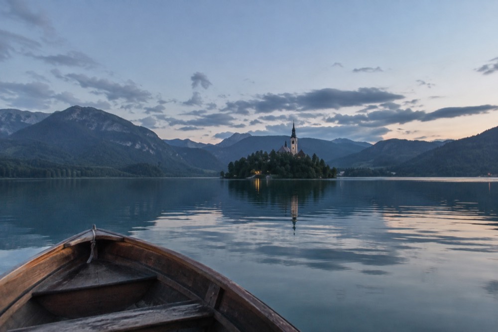 Small wooden boat on a calm alpine lake with a church on a small island