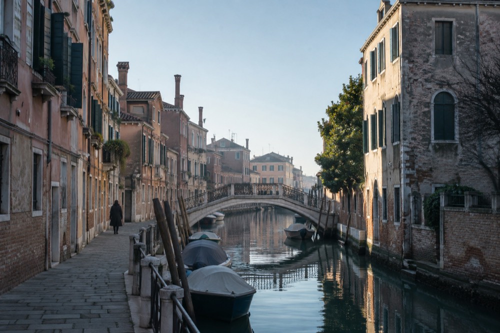 A quiet Venetian canal in morning light with stone bridges and shuttered buildings