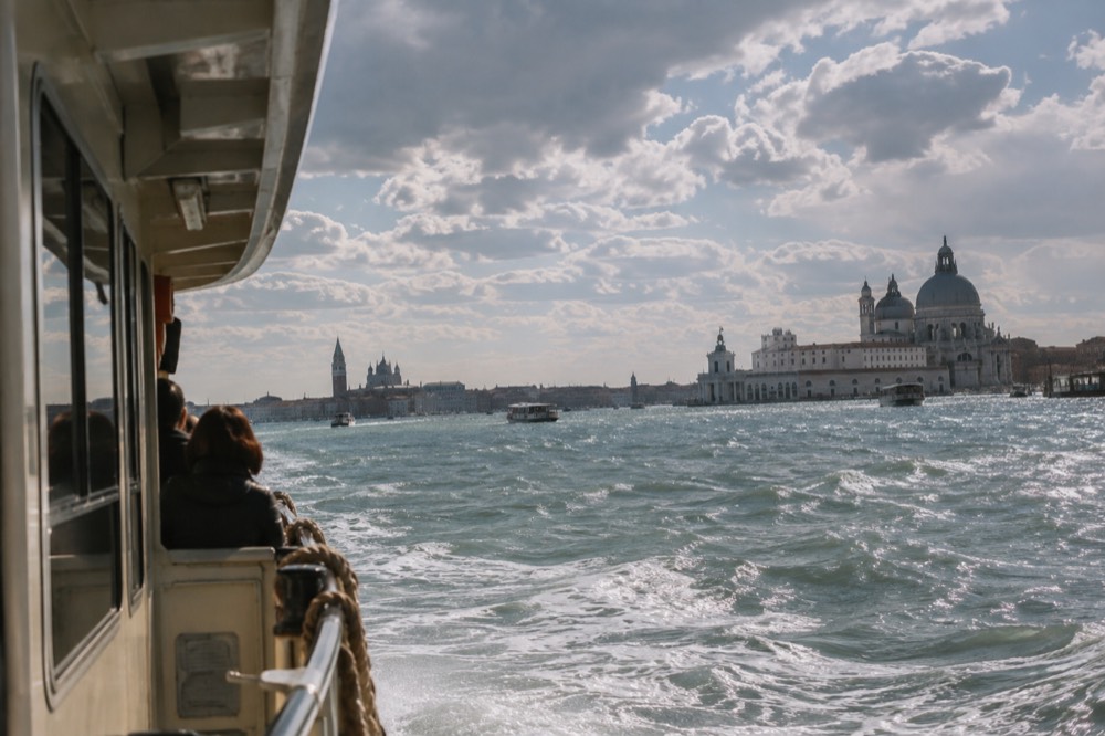 A water bus crossing the lagoon toward Venice with church domes on the horizon