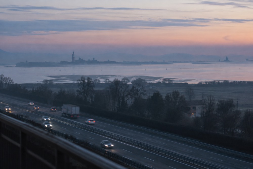 A motorway at dawn with hills in the distance and light fog over the fields