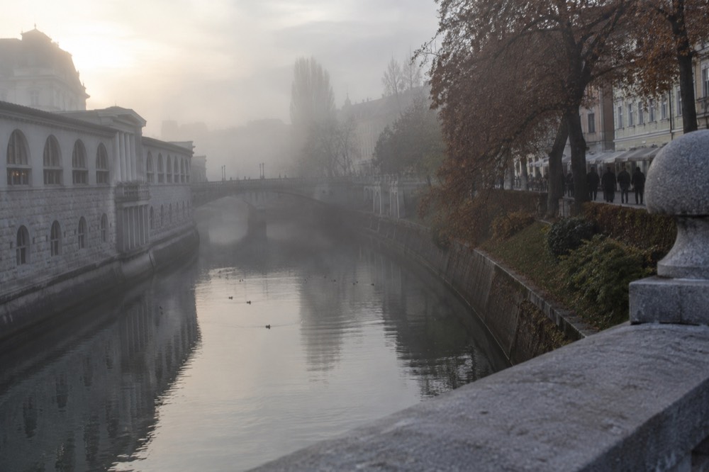 Autumn mist over the Ljubljanica river at dawn, with the city's bridges fading into fog