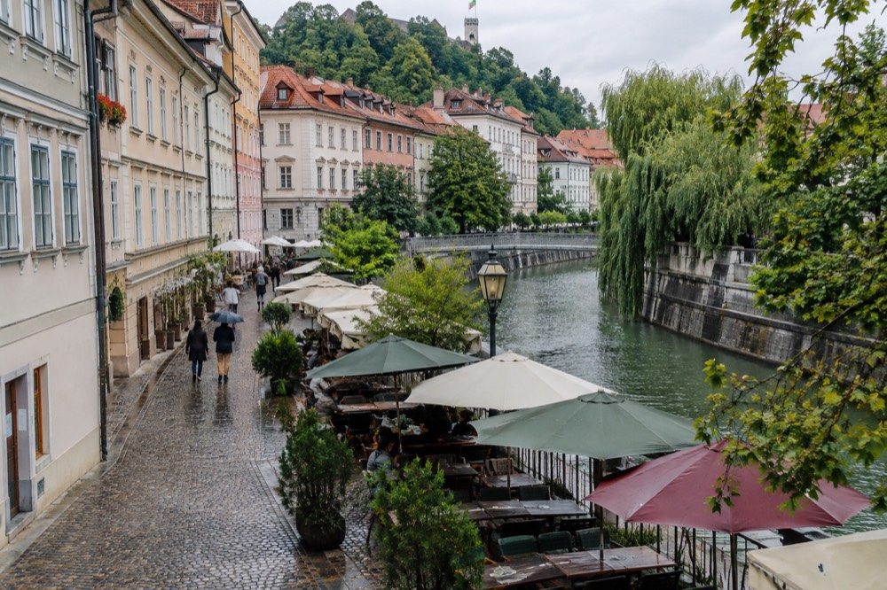 A packed outdoor table setting beside a riverfront street with umbrellas ready for rain