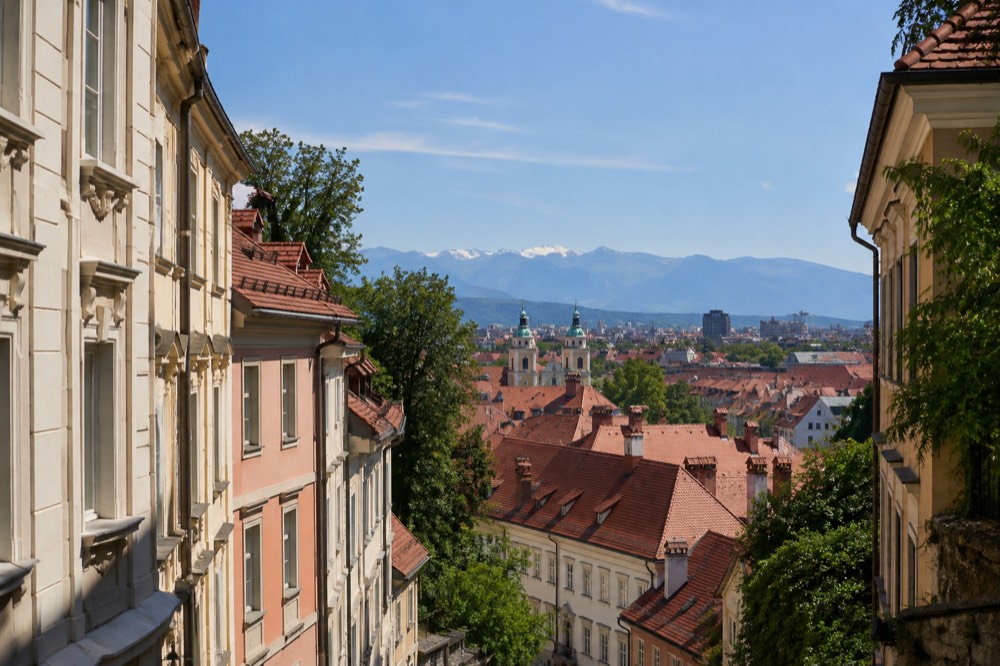 A view over the red rooftops of the old town towards the Julian Alps under clear sky
