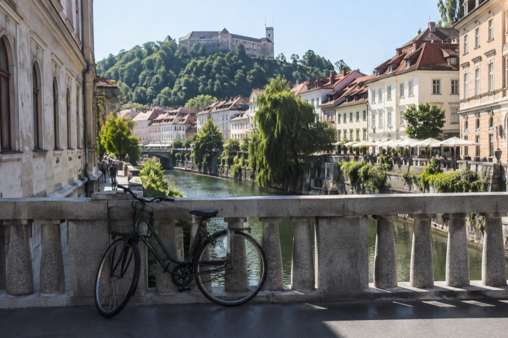 A bicycle leaning against a stone bridge railing with the river and a hilltop castle behind