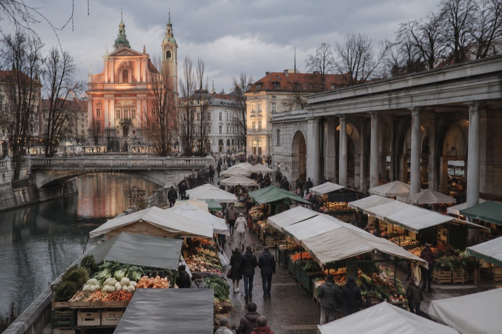 A city square under low grey cloud with bare trees and a lit church facade in winter