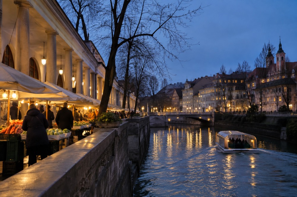 A small covered boat moving along a river between lit banks at dusk