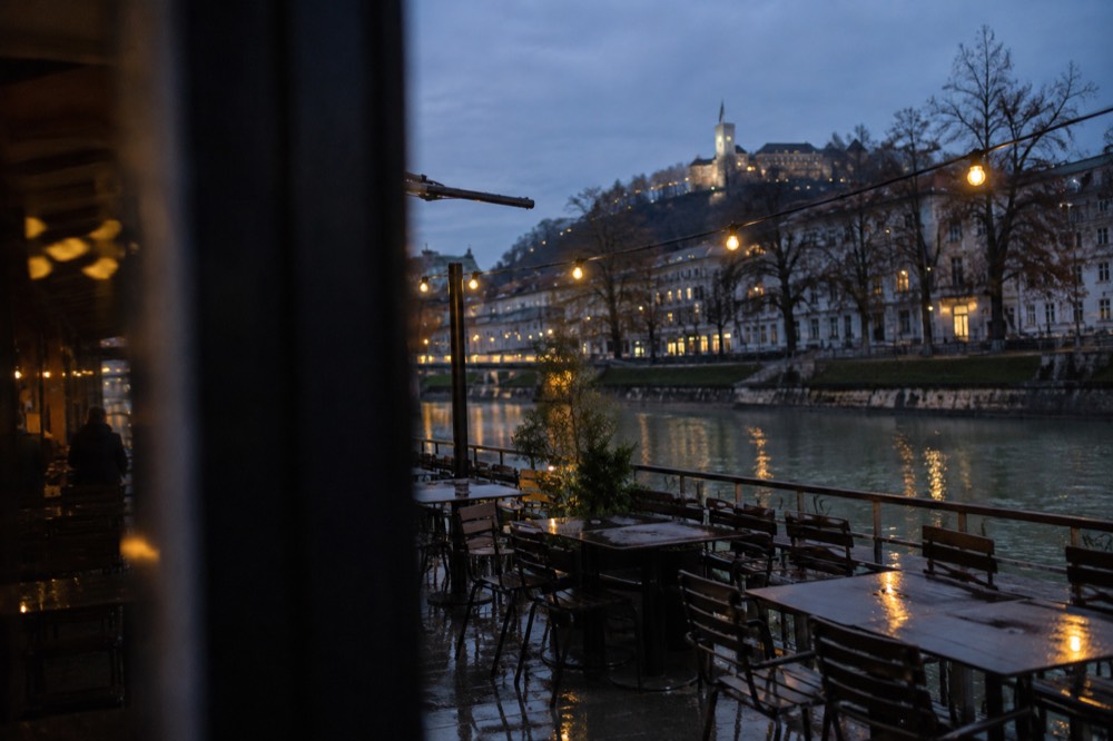 Empty terrace tables under string lights beside the river on an overcast evening