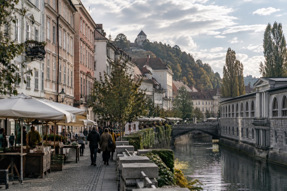 Market stalls and a covered colonnade beside the river in morning light