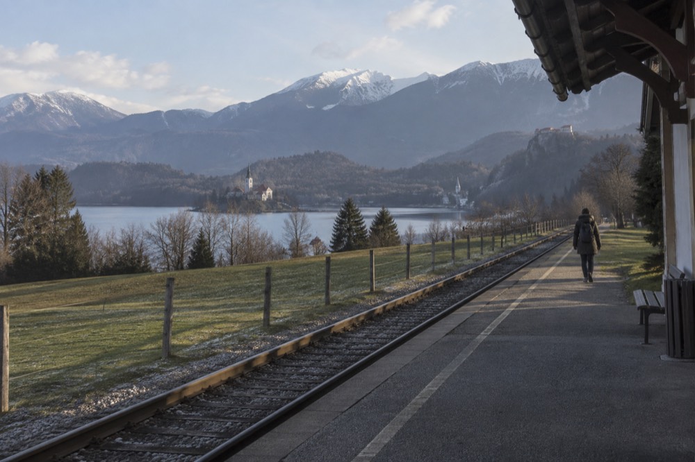 A rural railway platform beside green fields with forested hills in the distance
