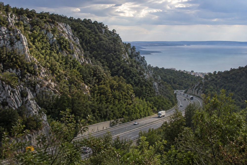 A motorway cutting through forested karst hills with limestone outcrops