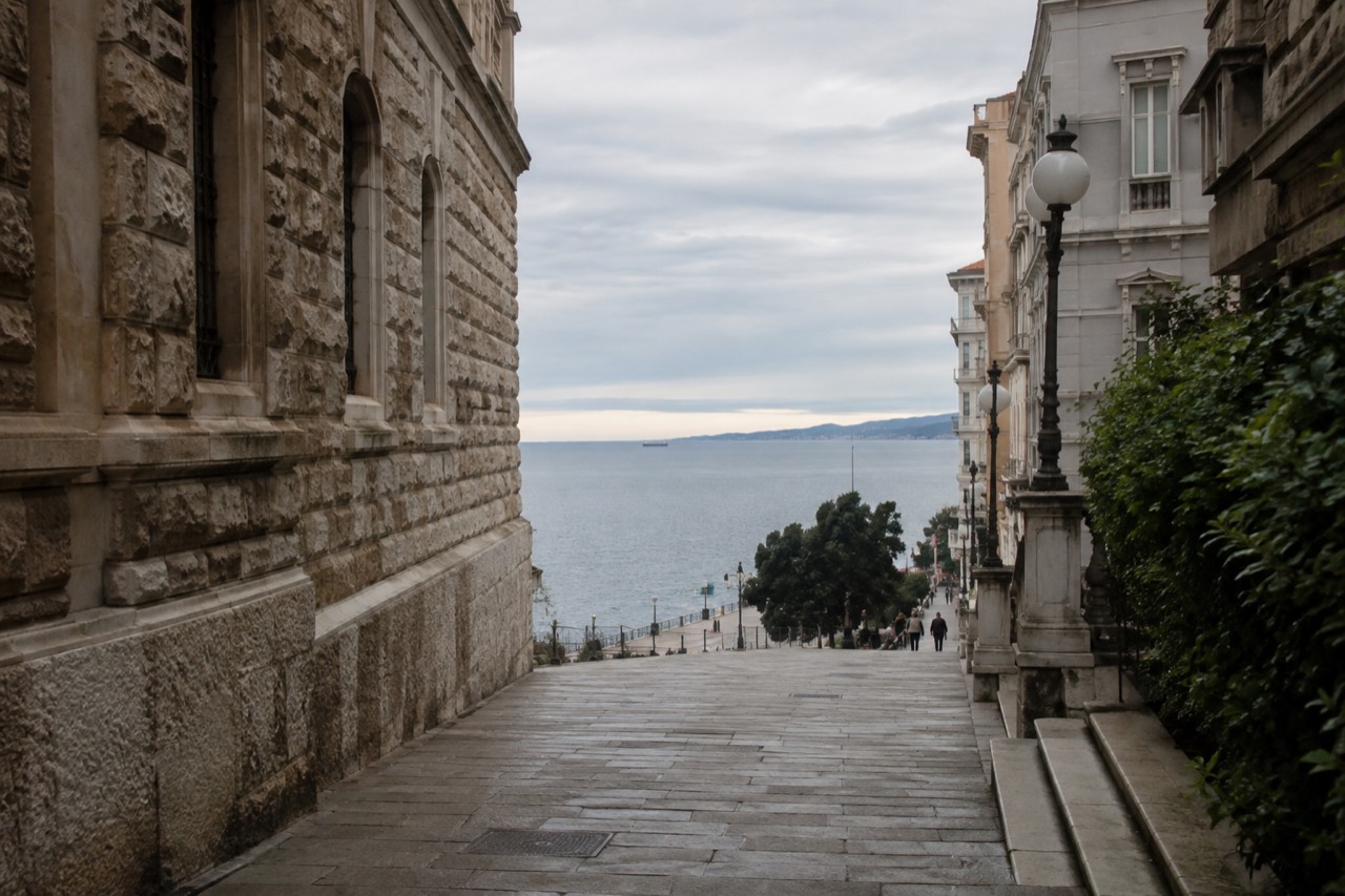 A coastal street with stone buildings leading down towards a sea horizon