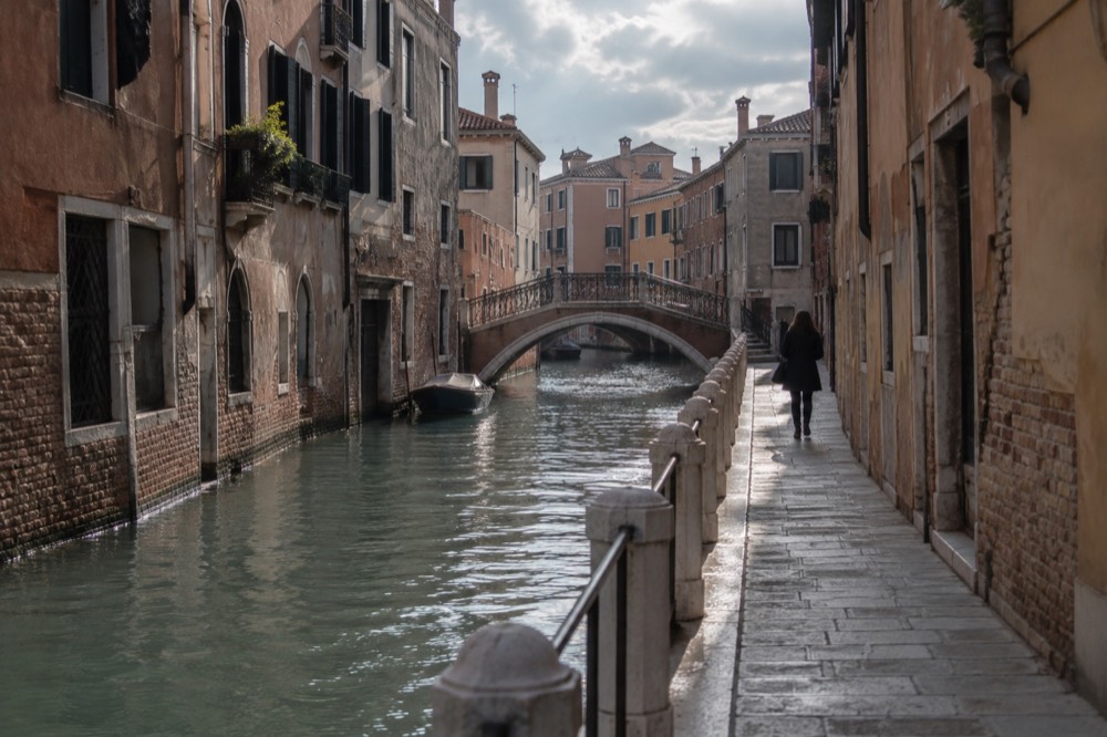 A quiet canal in Venice with an arched bridge and empty walkway in soft light
