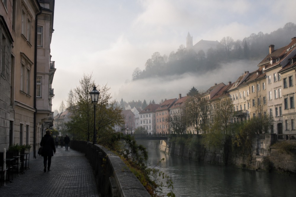Morning fog over rooftops of Ljubljana with a green hill rising above the mist