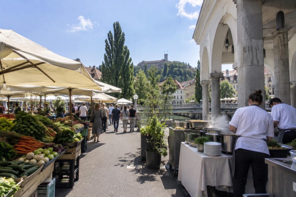 Chefs cooking at an open-air stall beside a stone market colonnade