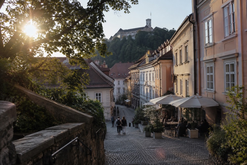 A cobbled old town lane rising towards Castle Hill, with pastel house fronts and café tables along the stone street