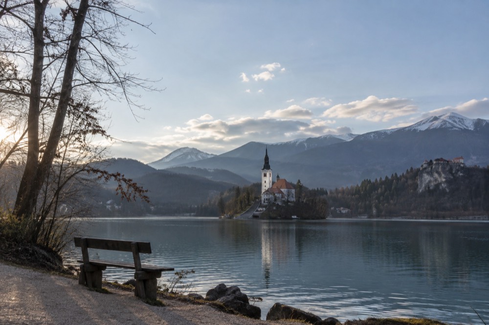 A lake ringed by forested hills with a small island church and a clifftop castle above the water