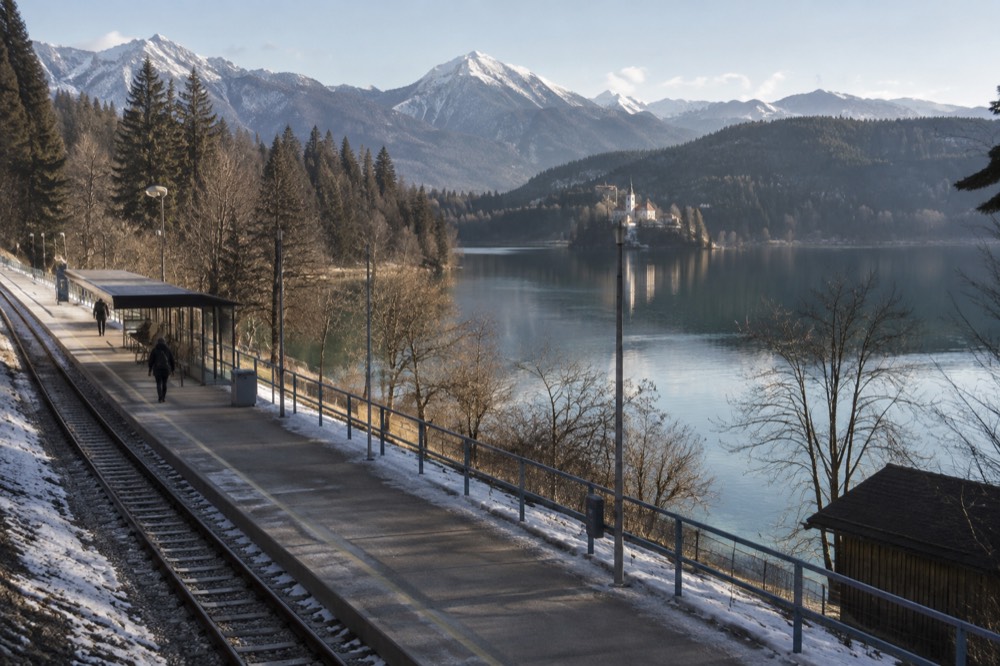 A small station platform beside Lake Bled with forested hills rising behind the water