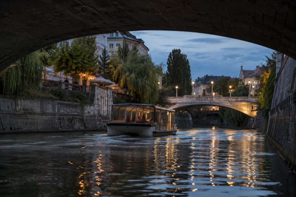 A river boat passing under a bridge on the Ljubljanica at dusk
