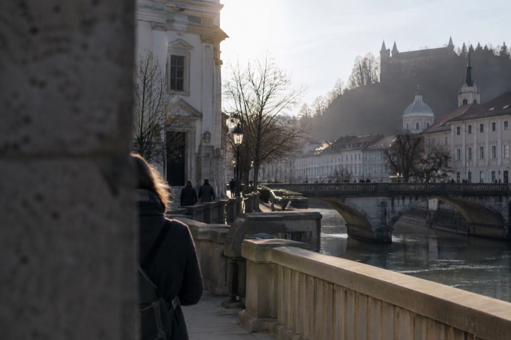 Pedestrian square with a church facade and riverside bridges in the background