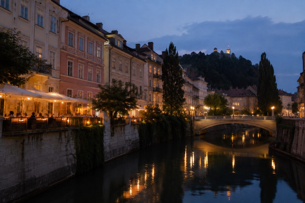 Illuminated bridges and riverside tables reflecting on dark water at dusk